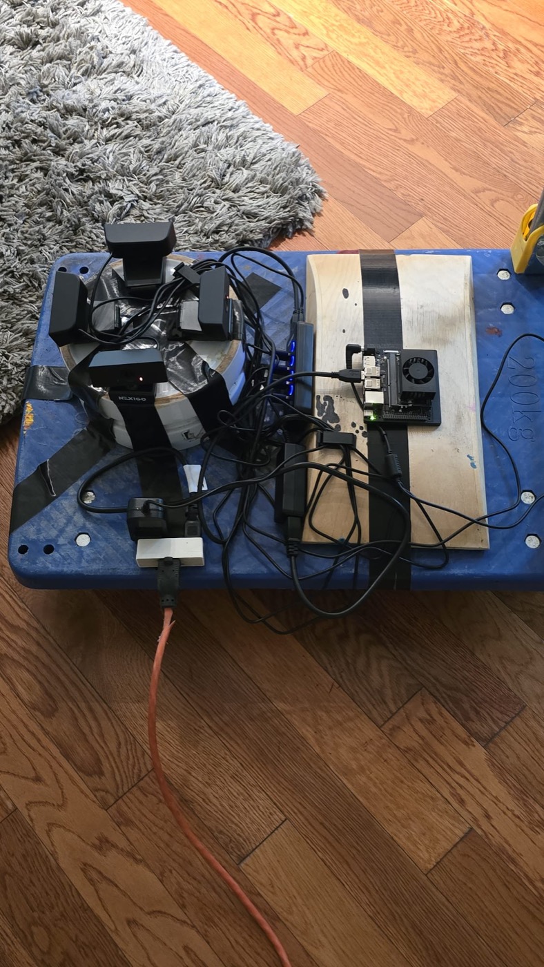 Four webcams on a drum, a USB hub and a Jetson Orin Nano strapped to a blue hand cart, one extension cord running off it.